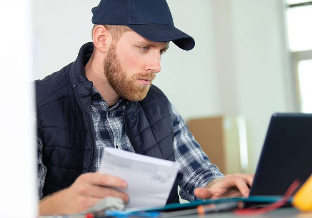 man in cap reading instructions and using laptop computer