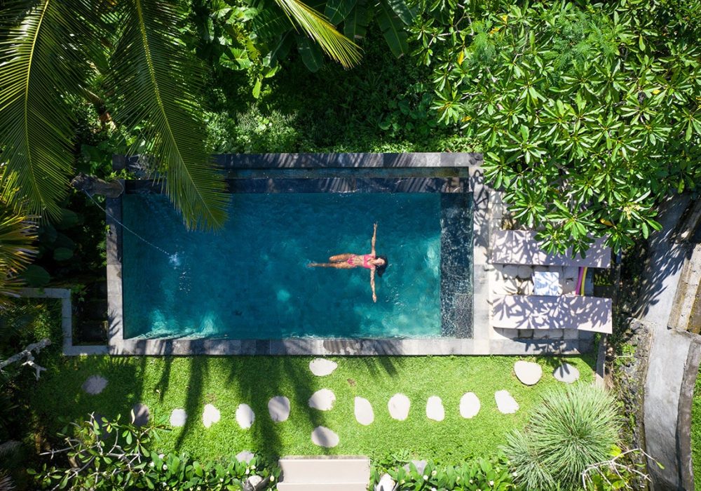 Beautiful girl relaxing outdoor in her garden with swimming pool. Summer concept about lifestyle,beauty, vacations and real estates. Aerial drone view